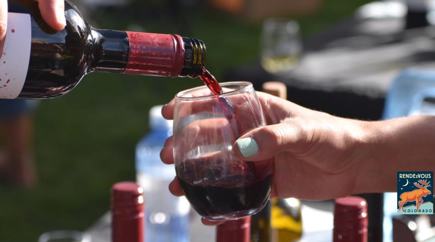 Person pouring red wine into a glass. RENDEZVOUS COLORADO logo